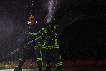 Image showing Firefighters using a water hose to eliminate a fire hazard. Team of female and male firemen in dangerous rescue mission.