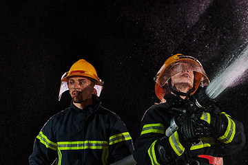 Image showing Firefighters using a water hose to eliminate a fire hazard. Team of female and male firemen in dangerous rescue mission.