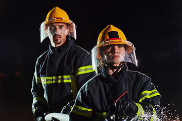 Image showing Firefighters using a water hose to eliminate a fire hazard. Team of female and male firemen in dangerous rescue mission.