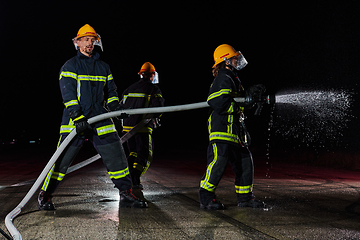 Image showing Firefighters using a water hose to eliminate a fire hazard. Team of female and male firemen in dangerous rescue mission.