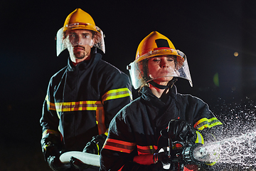 Image showing Firefighters using a water hose to eliminate a fire hazard. Team of female and male firemen in dangerous rescue mission.