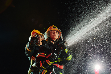 Image showing Firefighters using a water hose to eliminate a fire hazard. Team of female and male firemen in dangerous rescue mission.