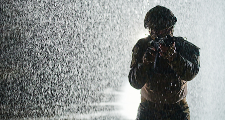 Image showing Army soldier in Combat Uniforms with an assault rifle, plate carrier and combat helmet going on a dangerous mission on a rainy night.