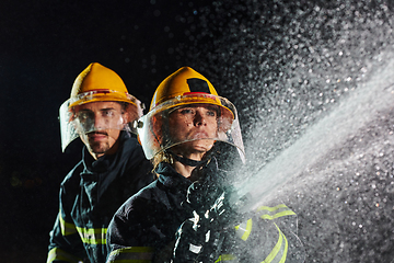 Image showing Firefighters using a water hose to eliminate a fire hazard. Team of female and male firemen in dangerous rescue mission.