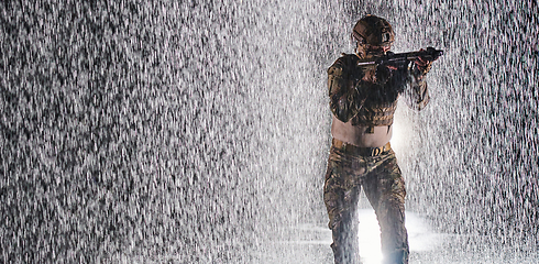 Image showing Army soldier in Combat Uniforms with an assault rifle, plate carrier and combat helmet going on a dangerous mission on a rainy night.