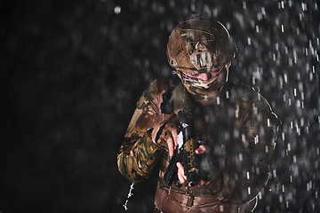 Image showing Army soldier in Combat Uniforms with an assault rifle, plate carrier and combat helmet going on a dangerous mission on a rainy night.