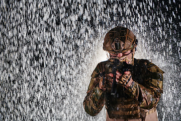 Image showing Army soldier in Combat Uniforms with an assault rifle, plate carrier and combat helmet going on a dangerous mission on a rainy night.