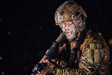 Image showing Army soldier in Combat Uniforms with an assault rifle, plate carrier and combat helmet going on a dangerous mission on a rainy night.