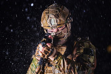 Image showing Army soldier in Combat Uniforms with an assault rifle, plate carrier and combat helmet going on a dangerous mission on a rainy night.