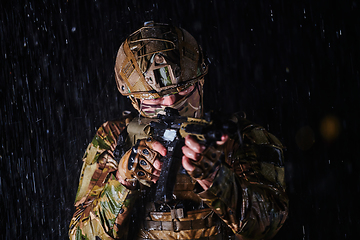 Image showing Army soldier in Combat Uniforms with an assault rifle, plate carrier and combat helmet going on a dangerous mission on a rainy night.