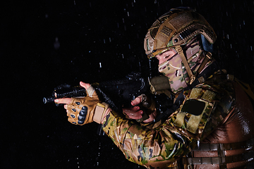 Image showing Army soldier in Combat Uniforms with an assault rifle, plate carrier and combat helmet going on a dangerous mission on a rainy night.