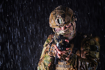 Image showing Army soldier in Combat Uniforms with an assault rifle, plate carrier and combat helmet going on a dangerous mission on a rainy night.