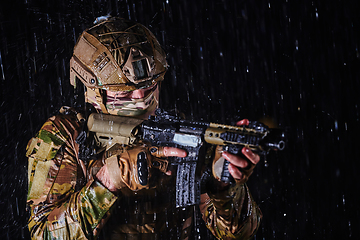 Image showing Army soldier in Combat Uniforms with an assault rifle, plate carrier and combat helmet going on a dangerous mission on a rainy night.