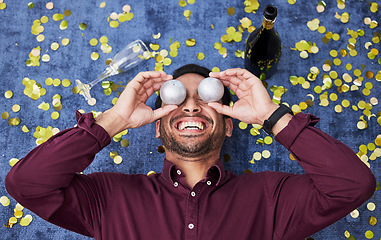 Image showing Christmas, drunk and funny with a man on the floor, laughing during a party or celebration event from above. Comic, comedy or festive with a happy young male person holding decorations over his face