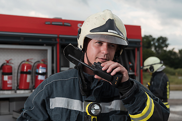 Image showing Fireman using walkie talkie at rescue action fire truck and fireman's team in background