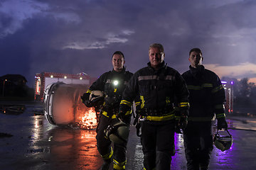 Image showing Brave Firefighters Team Walking to the Camera. In Background Paramedics and Firemen Rescue Team Fight Fire in Car Accident, Insurance and Save Peoples Lives concept.