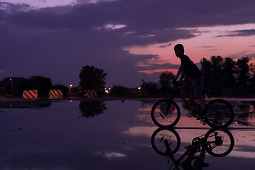 Image showing Lonely children silhouette on bike, boy riding bicycle on reflective water. Background beautiful sunset.