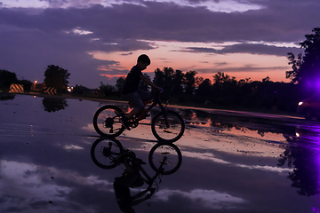 Image showing Lonely children silhouette on bike, boy riding bicycle on reflective water. Background beautiful sunset.