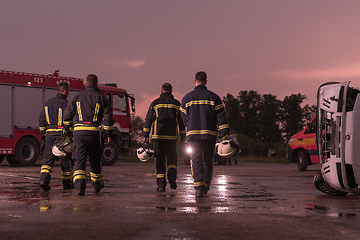 Image showing Brave Firefighters Team Walking to the Camera. In Background Paramedics and Firemen Rescue Team Fight Fire in Car Accident, Insurance and Save Peoples Lives concept.