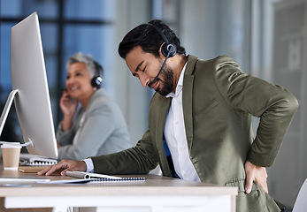 Image showing Back pain, call center and tired man with stress, burnout and fatigue at crm or contact us help desk. Asian agent or consultant person in telemarketing, sales and customer service with pain or injury