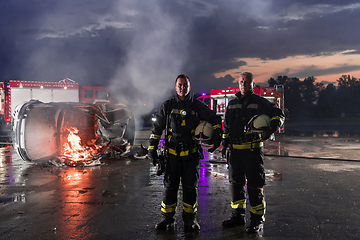 Image showing Brave Firefighters Team Walking to the Camera. In Background Paramedics and Firemen Rescue Team Fight Fire in Car Accident, Insurance and Save Peoples Lives concept.