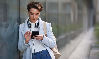 Image showing Woman, smartphone and social media with communication outdoor, chat or email with headphones, travel to work and mockup space. Young creative in city, mobile app with technology and 5g in Boston