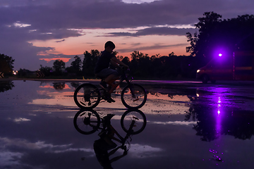 Image showing Lonely children silhouette on bike, boy riding bicycle on reflective water. Background beautiful sunset.