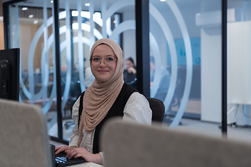 Image showing In a modern office, a young Muslim entrepreneur wearing a hijab sits confidently and diligently works on her computer, embodying determination, creativity, and empowerment in the business world