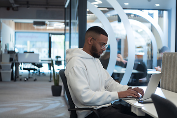 Image showing In a modern office setting, an African American businessman is diligently working on his laptop, embodying determination, ambition, and productivity in his professional environmen