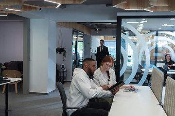 Image showing In a modern office African American young businessman and his businesswoman colleague, with her striking orange hair, engage in collaborative problem-solving sessions