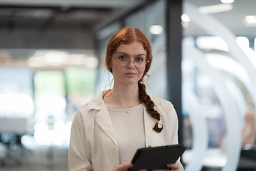 Image showing A young business woman with orange hair self-confident, fully engaged in working on a tablet, exuding creativity, ambition and a lively sense of individuality