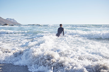 Image showing Surfing, man and swimming in sea waves, ocean and summer on blue sky in Cape Town, South Africa. Surfer guy, board and water sports at beach, relax and holiday for travel, adventure and sunny freedom