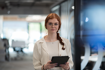 Image showing A young business woman with orange hair self-confident, fully engaged in working on a tablet, exuding creativity, ambition and a lively sense of individuality