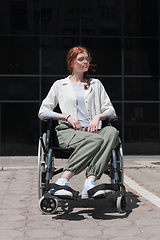 Image showing In front of a modern corporate building, a young woman sitting in a wheelchair confidently, symbolizing empowerment, inclusivity, and the strength to overcome challenges in the business world