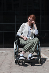 Image showing In front of a modern corporate building, a young woman sitting in a wheelchair confidently, symbolizing empowerment, inclusivity, and the strength to overcome challenges in the business world