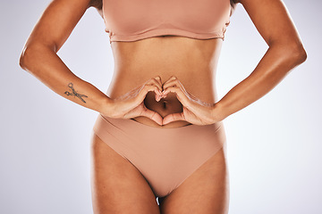 Image showing Health, body and woman with a heart in a studio for self love, wellness and positivity. Fitness, weightloss and slim female model with a love hand sign or gesture by her stomach by a gray background.