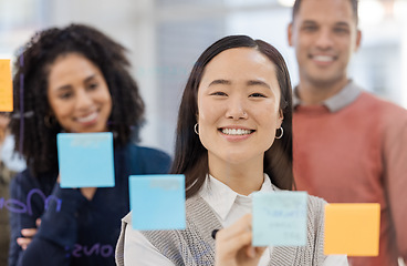 Image showing Asian woman, portrait smile and writing schedule in planning, strategy or brainstorming on glass wall at office. Happy female designer in teamwork project plan, tasks or post it with sticky note