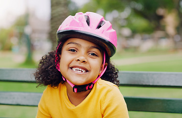 Image showing Girl child, portrait and helmet while happy outdoor on a park bench with a smile for safety gear. Face of black kid in nature learning to ride a bicycle while on summer vacation or holiday for health