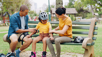 Image showing Parents, park bench and helmet with kid, help and safety for skating, rollerskate or bike. Interracial family, mom and dad with helping hand, teaching and girl kid for bonding, learning and exercise