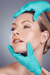 Image showing Woman, studio and surgeon hands for cosmetic surgery, facial transformation and beauty by gray background. Model, anti aging and headshot with consulting, skincare and inspection for face aesthetic