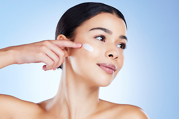 Image showing Woman, face and hand for skincare moisturizer in cosmetics or beauty against a blue studio background. Female applying product, lotion or cream for facial treatment, collagen or healthy self care
