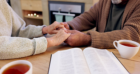 Image showing Bible study, senior couple and holding hands for praying, religion and closeup in home for mindfulness. Elderly person, book and hope for peace, gratitude or connection to God, holy spirit or faith