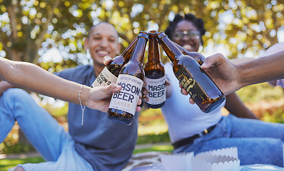 Image showing Closeup, picnic and toast beer with friends on grass, happiness and together in nature, park or outdoor. Summer, happy time and diversity for cheers with bottle, craft beer and alcohol with people
