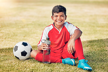 Image showing Soccer, children and water with a ball and boy child sitting on a grass pitch or field after training. Football, fitness and hydration with a young male kid at a sports venue, stadium or arena