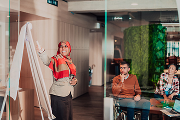 Image showing An older Muslim businesswoman presents a project to a young diverse team of people in a modern office