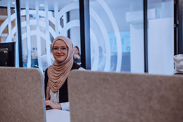 Image showing In a modern office, a young Muslim entrepreneur wearing a hijab sits confidently and diligently works on her computer, embodying determination, creativity, and empowerment in the business world