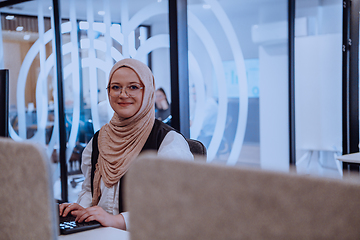 Image showing In a modern office, a young Muslim entrepreneur wearing a hijab sits confidently and diligently works on her computer, embodying determination, creativity, and empowerment in the business world