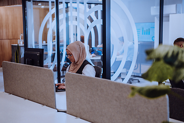 Image showing In a modern office, a young Muslim entrepreneur wearing a hijab sits confidently and diligently works on her computer, embodying determination, creativity, and empowerment in the business world