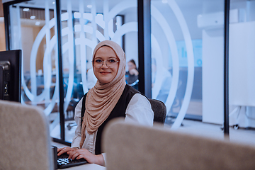 Image showing In a modern office, a young Muslim entrepreneur wearing a hijab sits confidently and diligently works on her computer, embodying determination, creativity, and empowerment in the business world