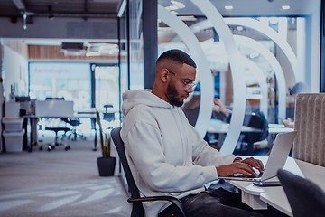 Image showing In a modern office setting, an African American businessman is diligently working on his laptop, embodying determination, ambition, and productivity in his professional environmen